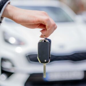 Close-up of a hand holding a car key, with a white car in the background outdoors.