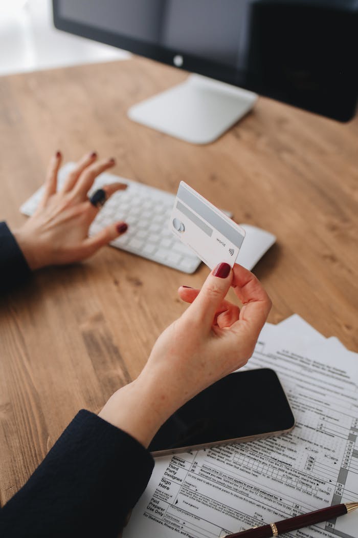 Woman's hand with credit card and manicured nails typing on keyboard. Modern business setup.