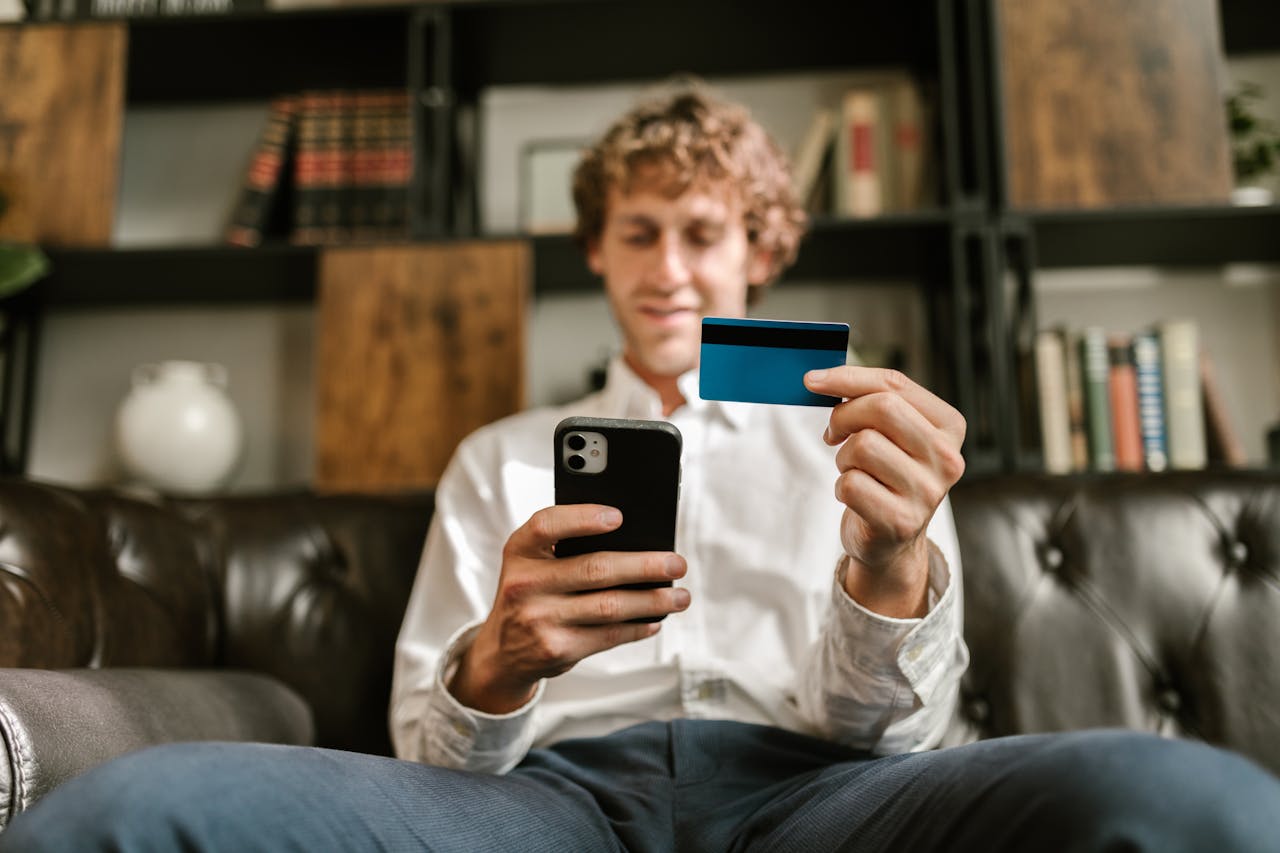 A man smiles while using his smartphone and credit card for online shopping.